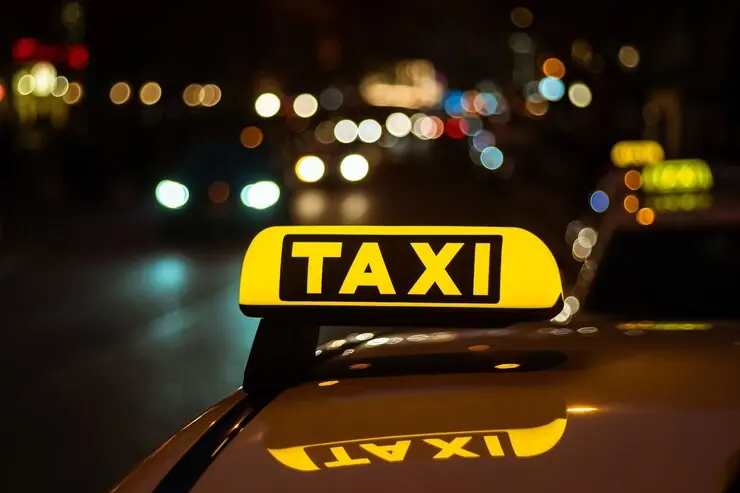 Lampa galbenă TAXI aprinsă pe acoperișul unei mașini, noaptea