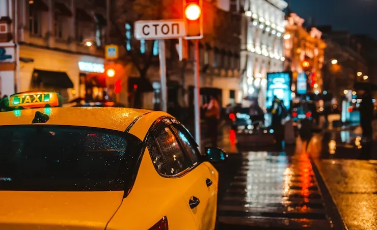Taxi galben oprit seara pe o stradă udă din oraș, cu luminile vitrinelor reflectate în asfalt